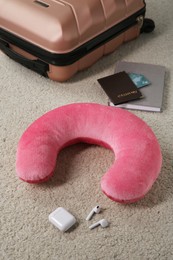 Photo of Pink travel pillow, suitcase, passport with credit cards and earphones on beige rug