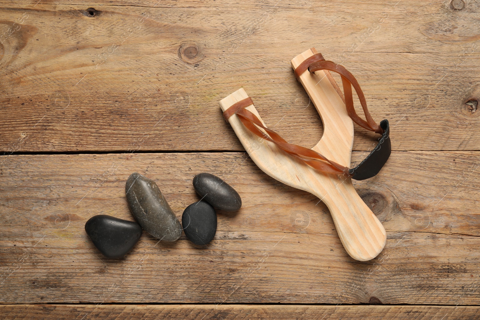 Photo of Slingshot with stones on wooden background, flat lay