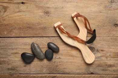 Slingshot with stones on wooden background, flat lay