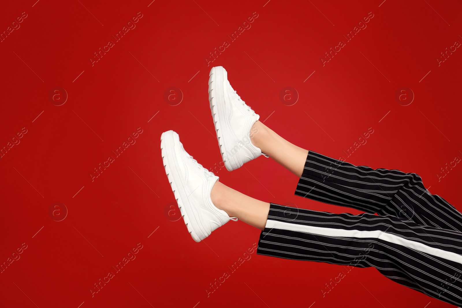 Photo of Woman in stylish sport shoes on red background