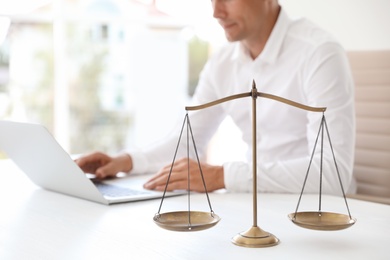 Photo of Scales of justice and blurred notary with laptop on background