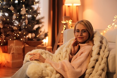 Photo of Young woman with plaid near sofa at home, space for text. Christmas celebration