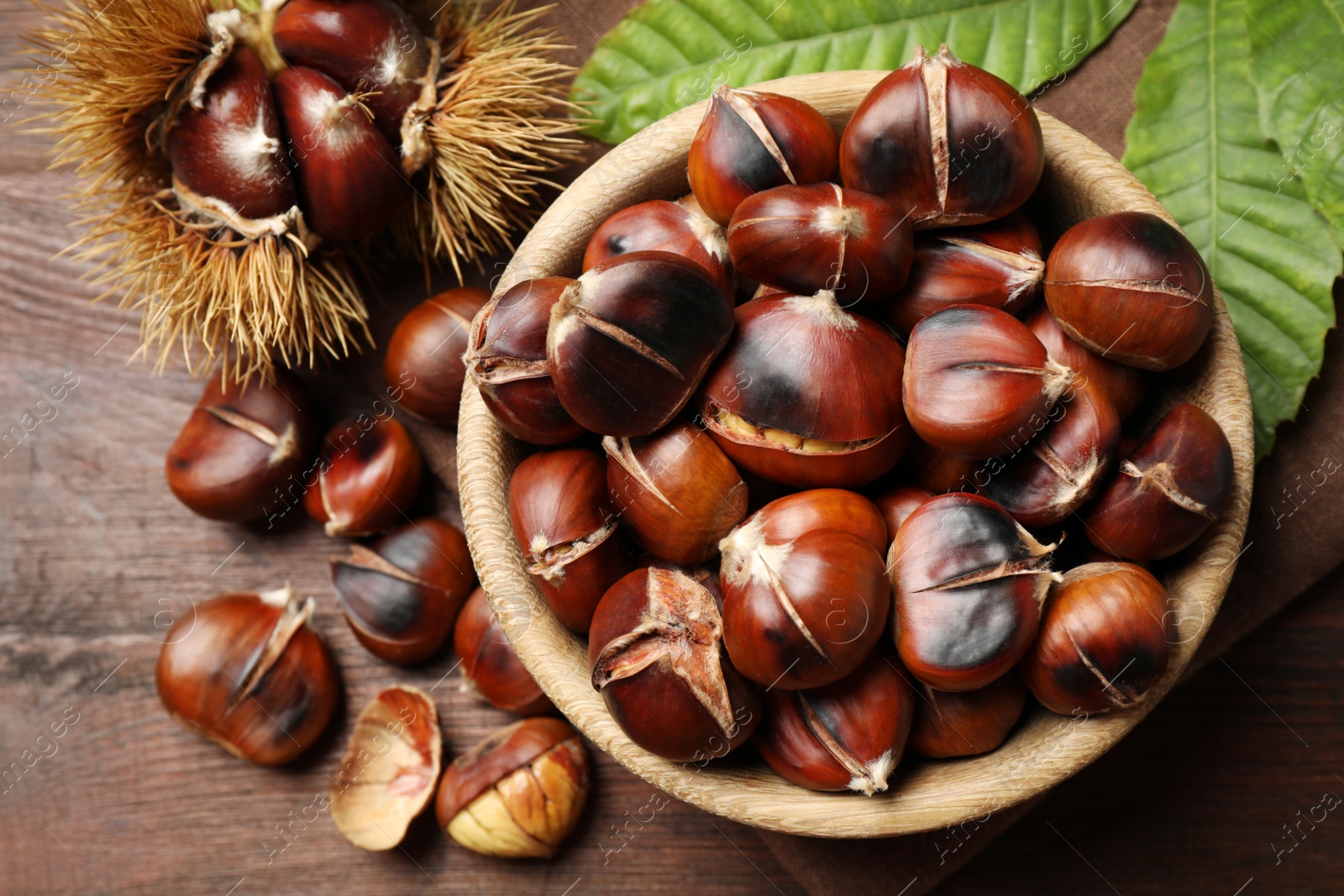Photo of Delicious roasted edible chestnuts on brown wooden table, flat lay
