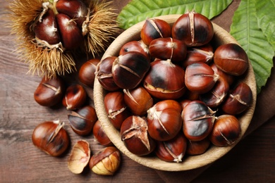 Photo of Delicious roasted edible chestnuts on brown wooden table, flat lay