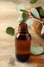 Bottle of eucalyptus essential oil and leaves on wooden table