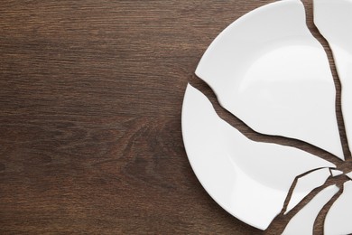 Photo of Pieces of broken ceramic plate on wooden table, flat lay. Space for text