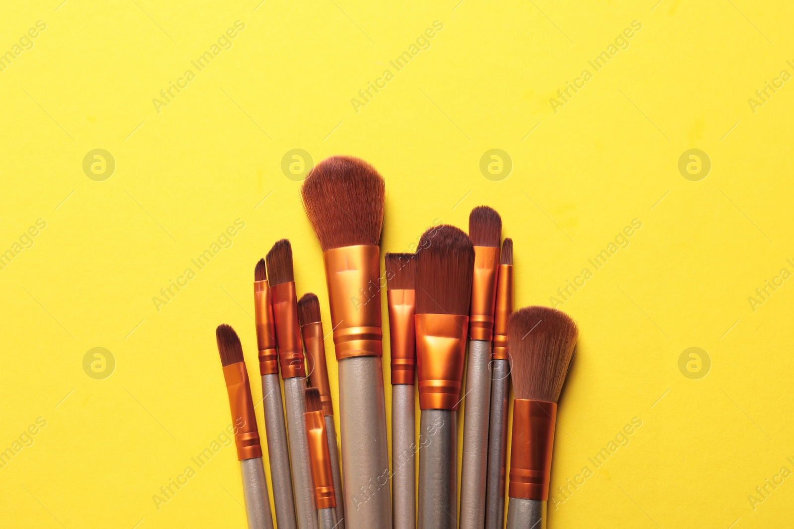 Photo of Different makeup brushes on yellow background, flat lay. Space for text