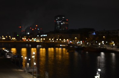 Blurred view of cityscape with bridge over river and buildings at night