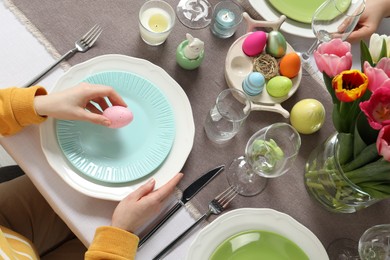 Woman setting table for festive Easter dinner at home, top view