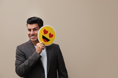 Happy man holding card with drawn smiling face on beige background. Space for text