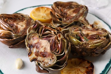 Photo of Plate with tasty grilled artichokes on white table, closeup