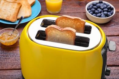 Photo of Yellow toaster with roasted bread, blueberries and jam on wooden table, closeup