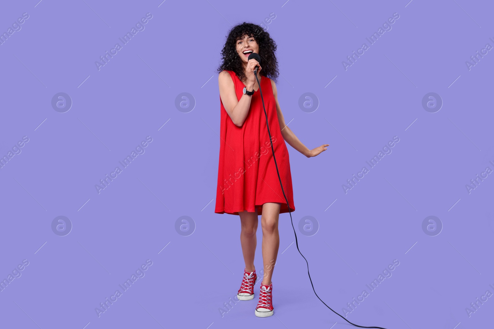 Photo of Beautiful young woman with microphone singing on purple background