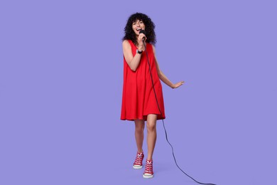 Photo of Beautiful young woman with microphone singing on purple background