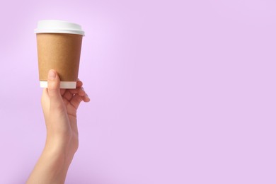 Woman holding takeaway paper coffee cup on violet background, closeup. Space for text