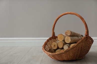 Wicker basket with firewood near grey wall indoors, space for text