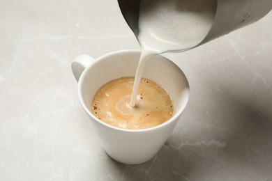 Photo of Pouring milk into cup of coffee on grey table, closeup