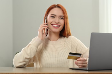 Photo of Happy woman with credit card using smartphone for online shopping at wooden table indoors