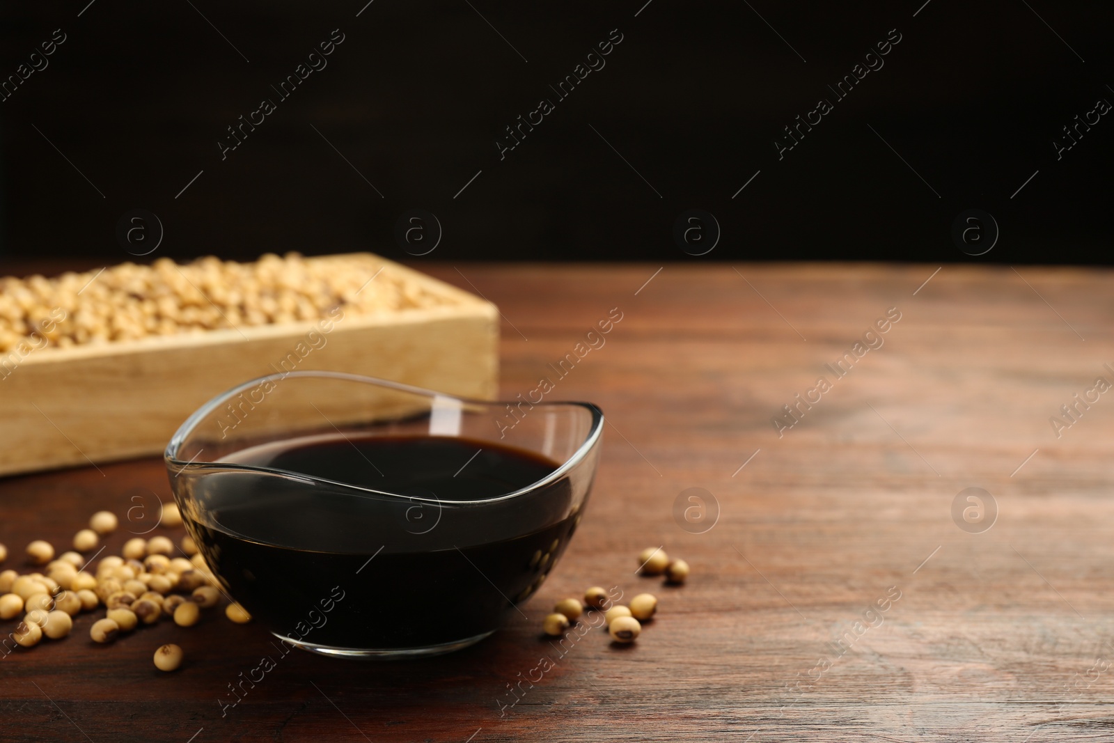 Photo of Soy sauce in bowl and soybeans on wooden table. Space for text