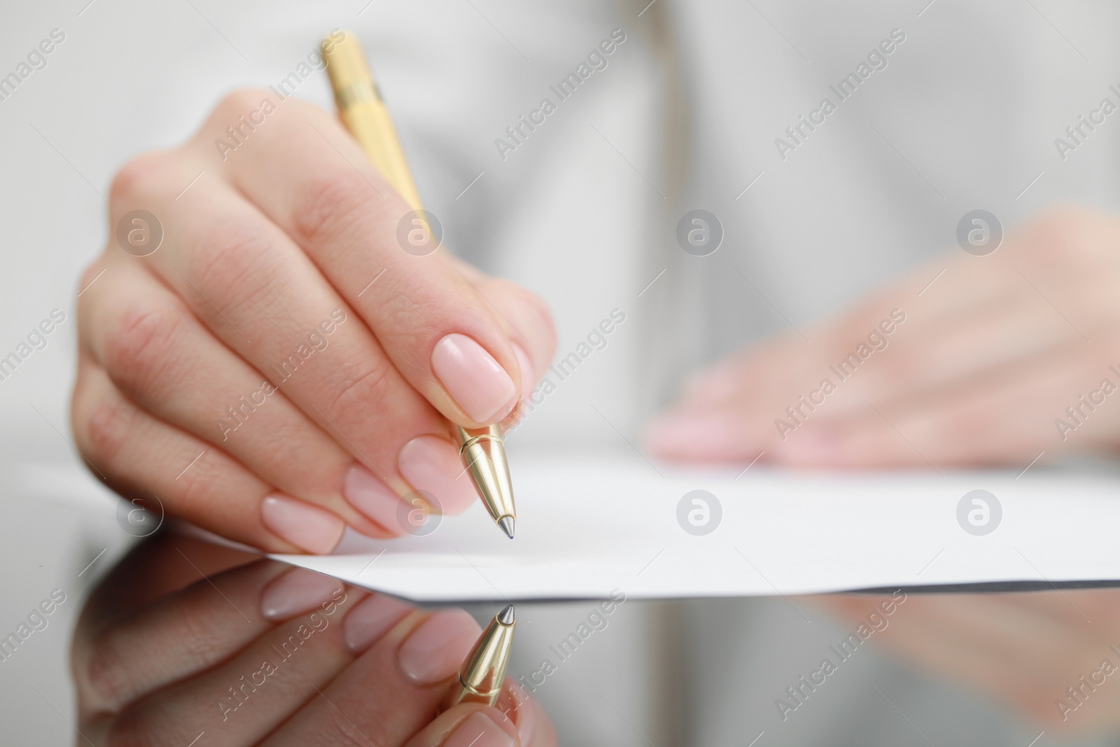 Photo of Woman writing on sheet of paper at glass table, closeup