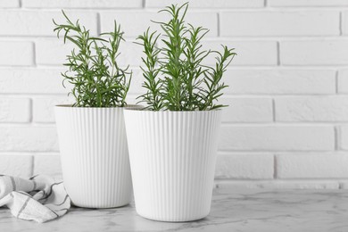 Beautiful green potted rosemary on white marble table near brick wall, space for text