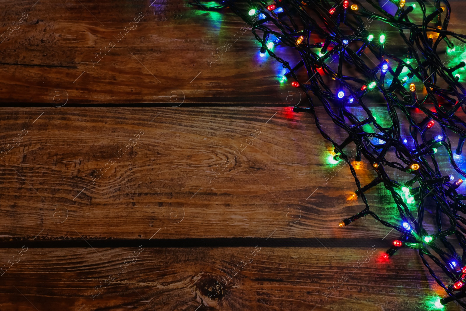 Photo of Glowing festive lights on wooden table, top view. Space for text