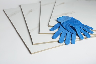 Stack of ceramic tiles and gloves on white background. Space for text