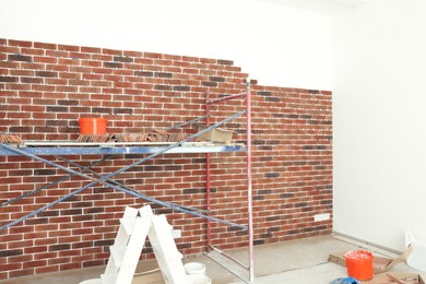 Scaffolding near wall with decorative bricks and tile leveling system in room