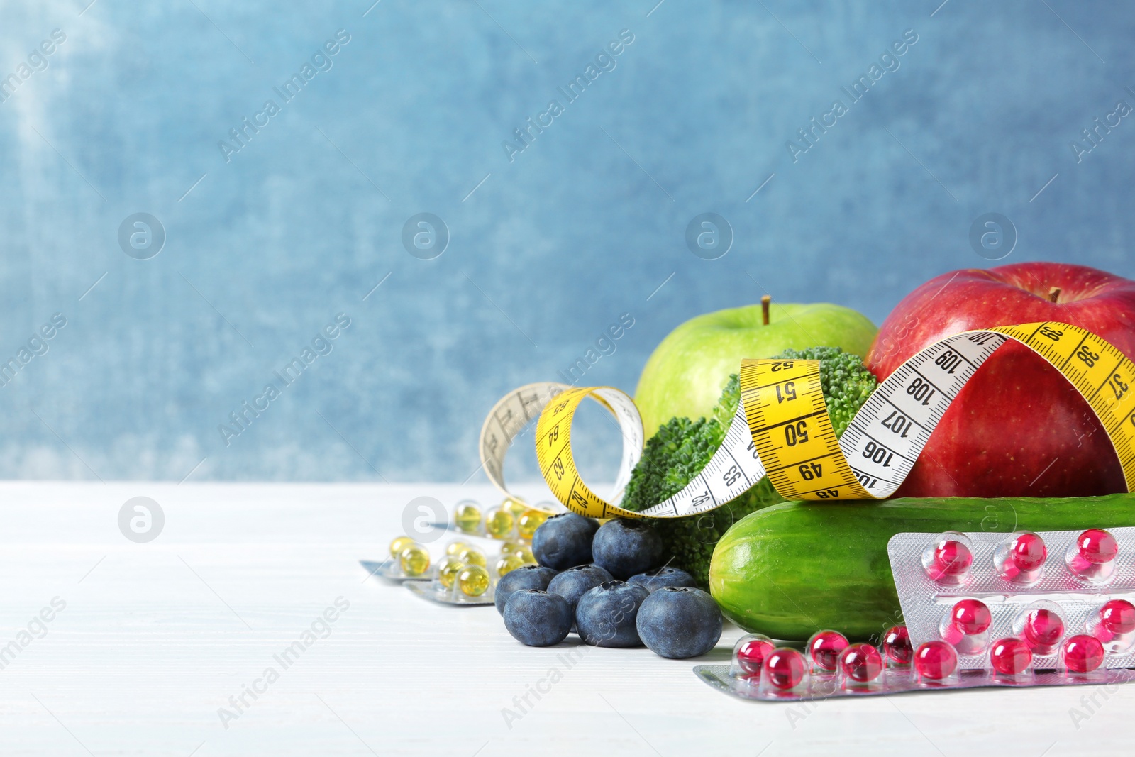 Photo of Weight loss pills with measuring tape and healthy food on light table. Space for text