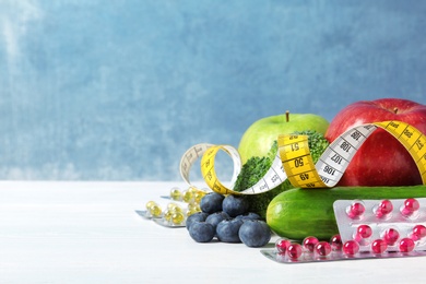 Photo of Weight loss pills with measuring tape and healthy food on light table. Space for text