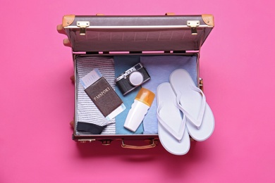 Photo of Open vintage suitcase with beach objects on pink background, top view