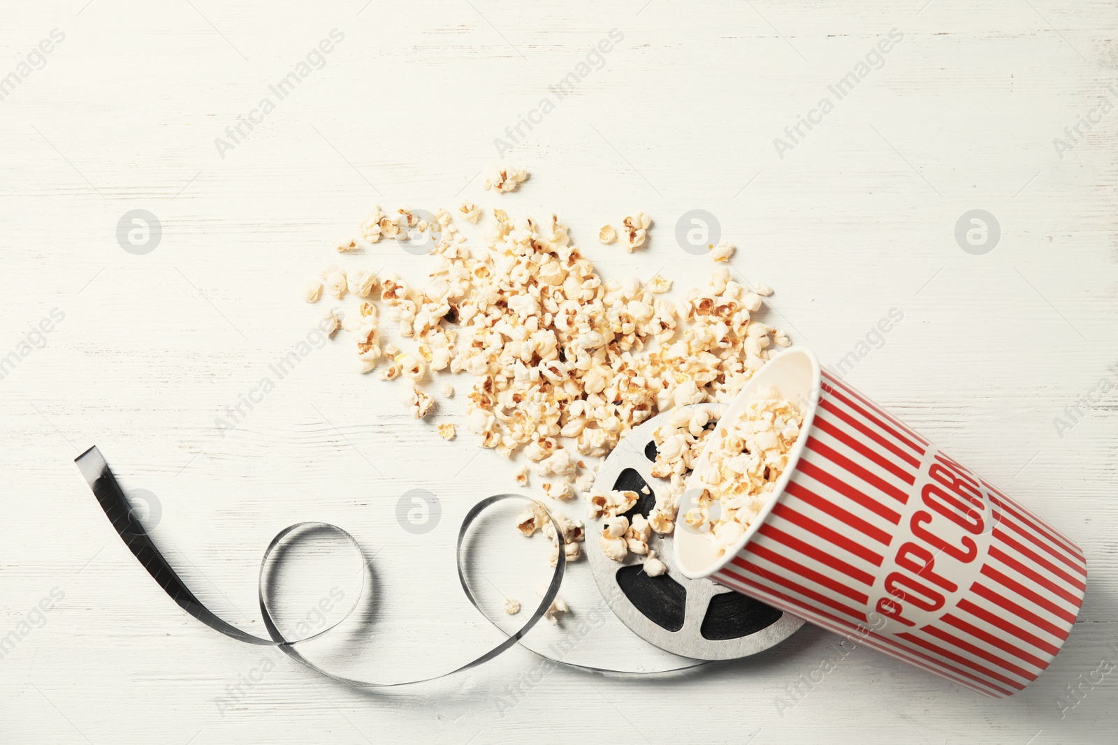 Photo of Tasty popcorn and film reel on wooden background, top view. Cinema snack