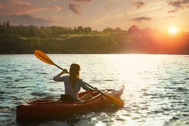 Woman kayaking on river at sunset, back view. Summer activity