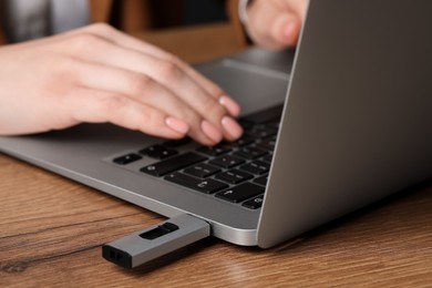 Woman using laptop with attached usb flash drive at wooden table, closeup