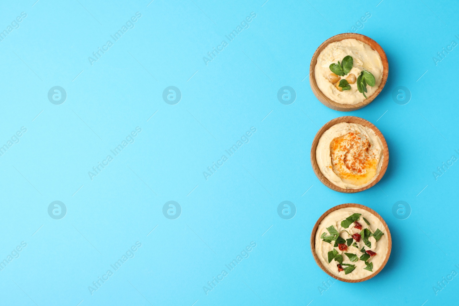 Photo of Different kinds of tasty hummus in bowls on light blue background, flat lay. Space for text