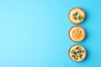 Photo of Different kinds of tasty hummus in bowls on light blue background, flat lay. Space for text