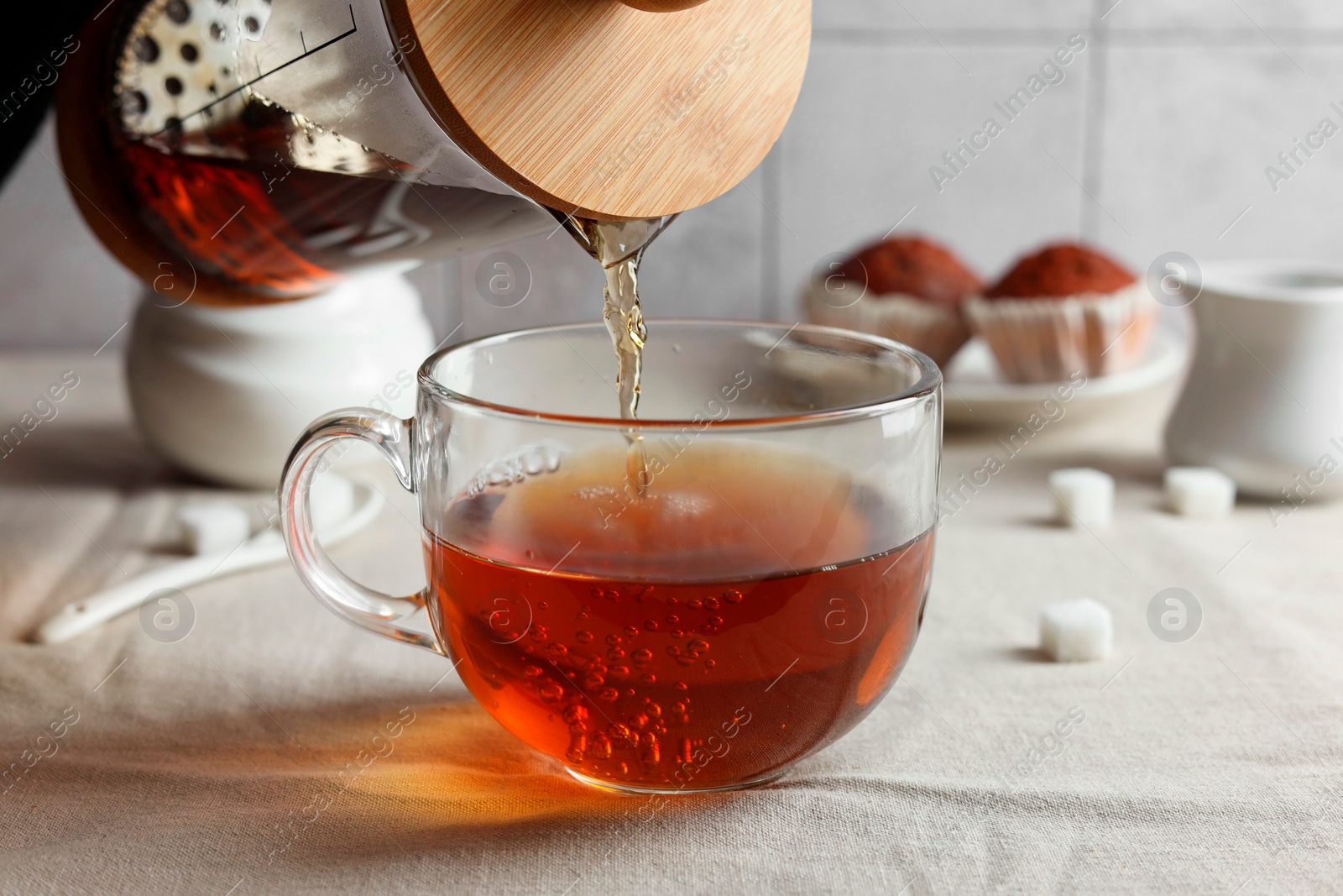 Photo of Pouring warm tea into cup on light table, closeup