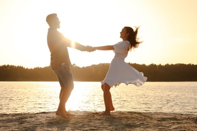 Happy couple dancing near river at sunset