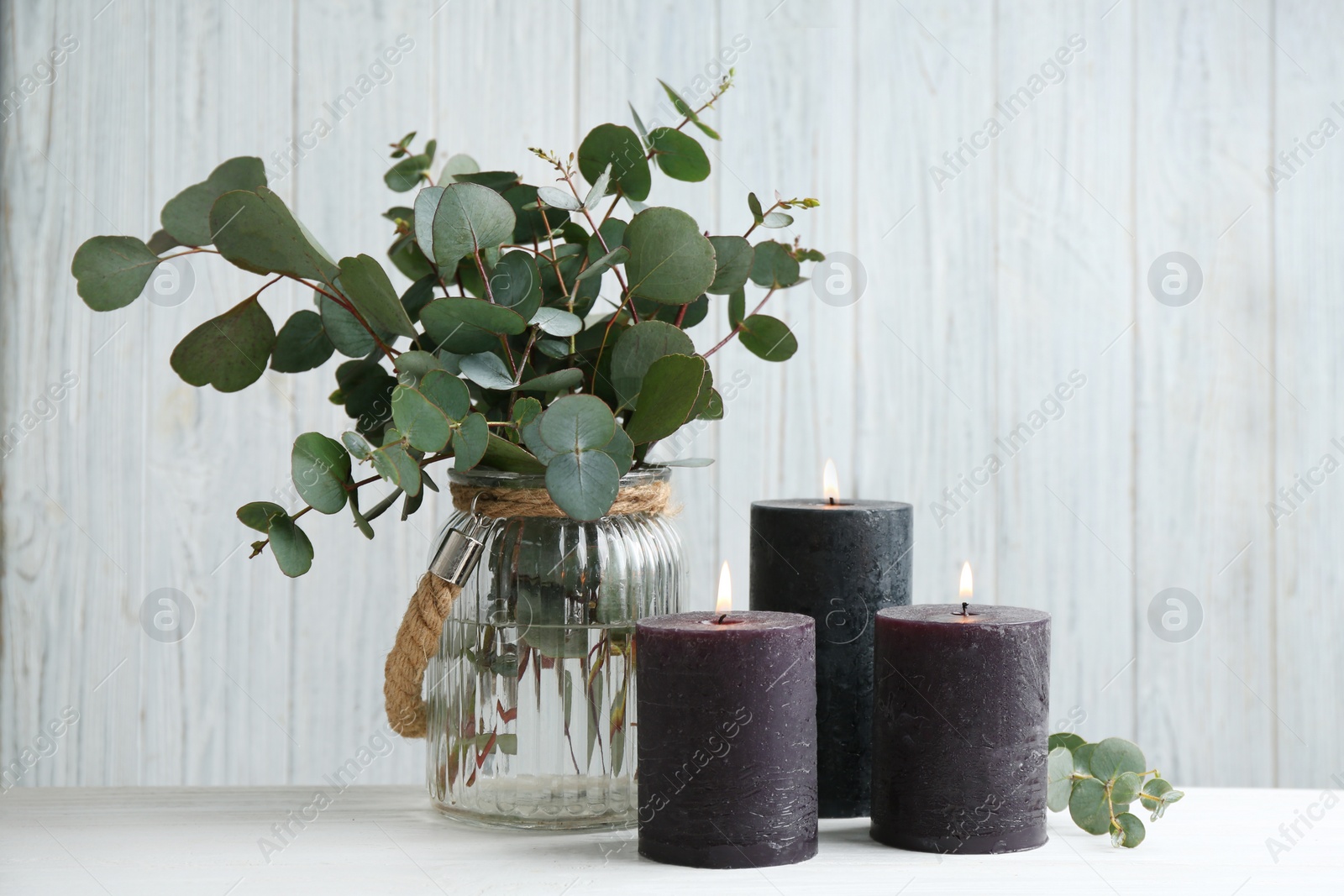 Photo of Burning candles and green branches on white table