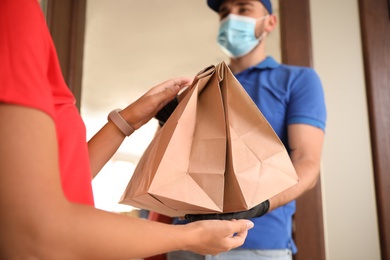 Courier in protective mask and gloves giving order to woman at entrance, focus on hands. Restaurant delivery service during coronavirus quarantine