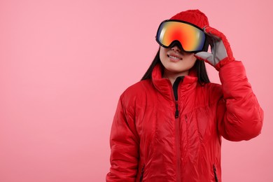 Happy woman in winter sportswear and goggles on pink background. Space for text