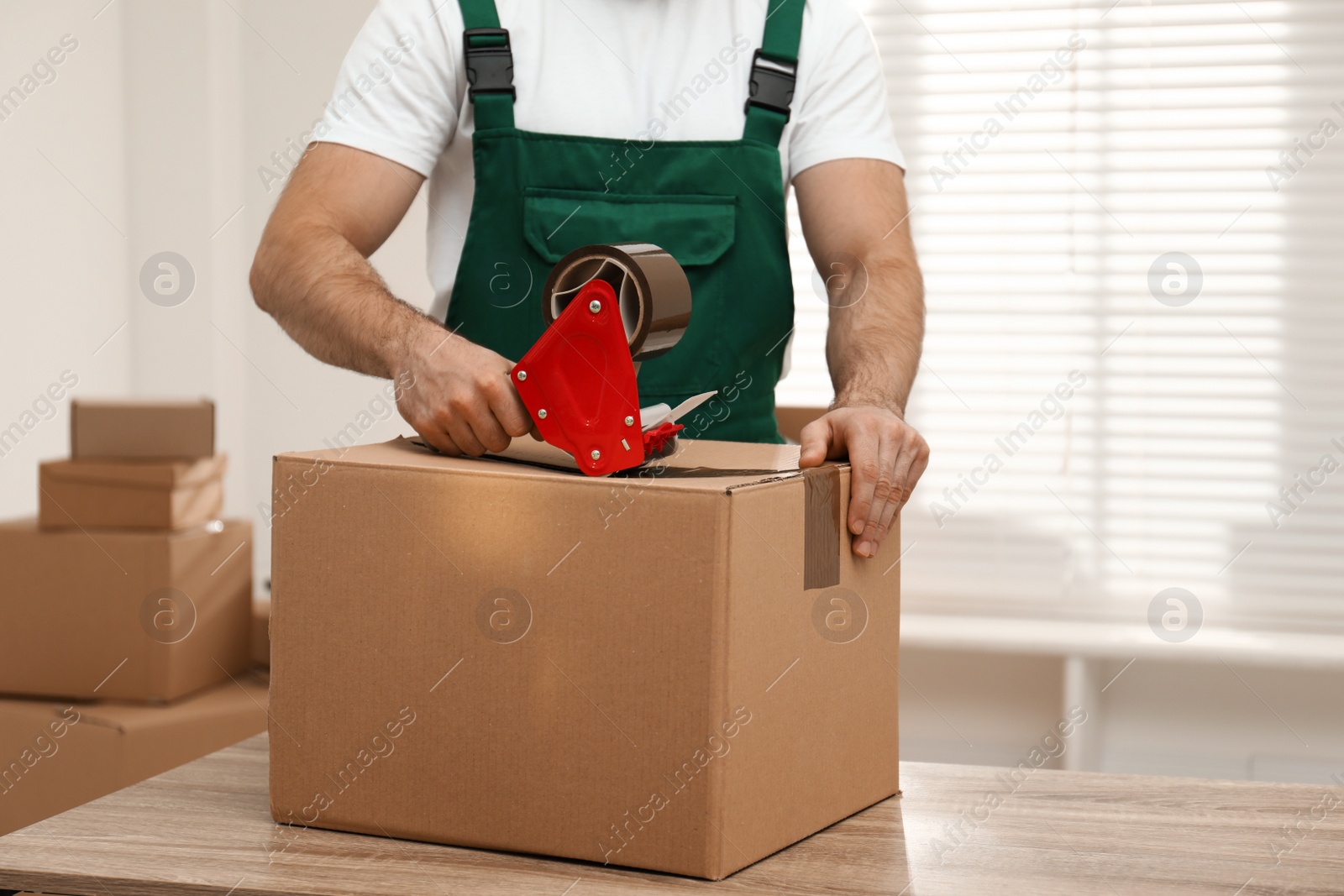 Photo of Man packing box with adhesive tape indoors, closeup. Moving service