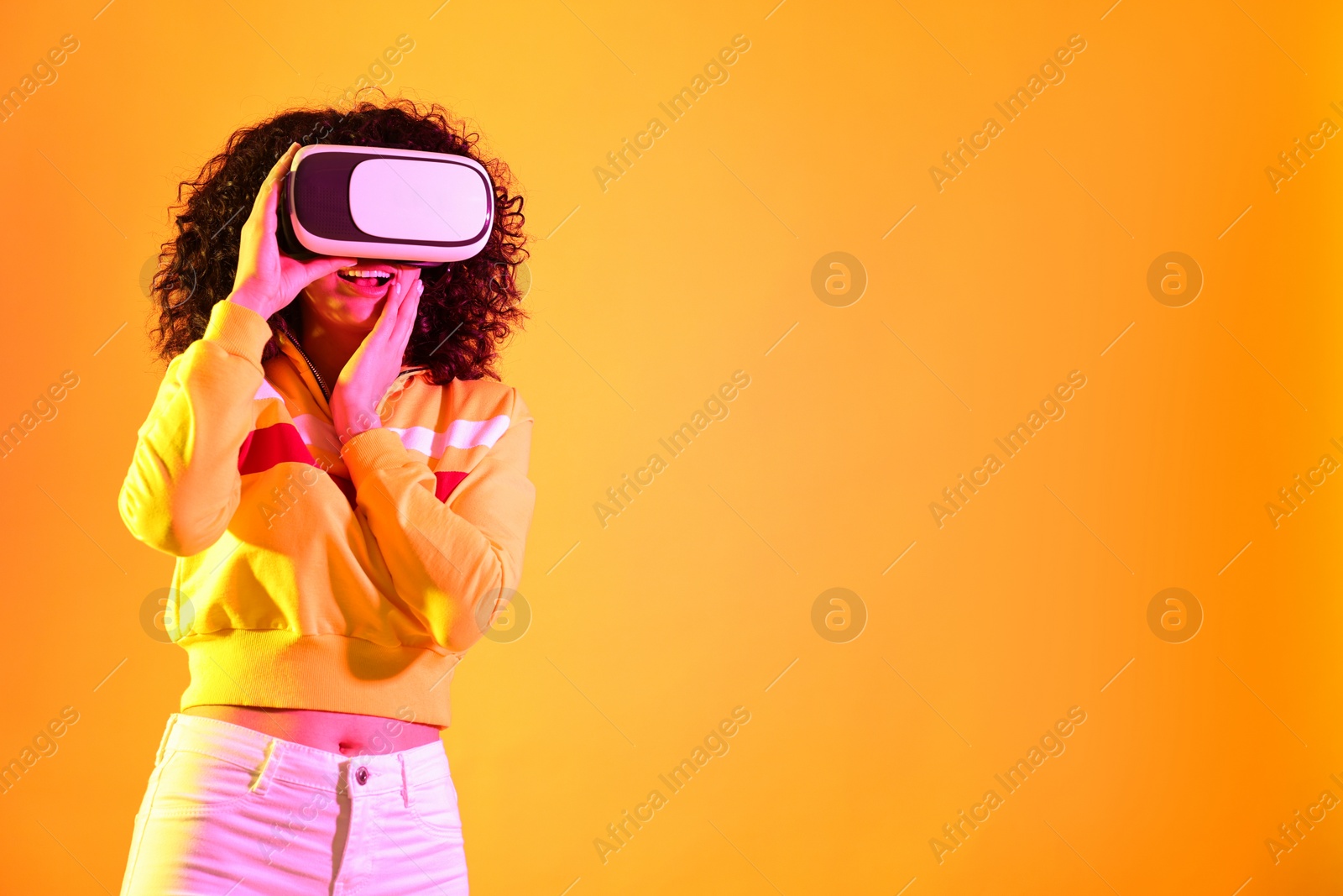 Photo of Beautiful young woman with virtual reality headset on color background in neon lights