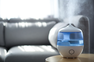 Photo of Modern air humidifier on table in living room. Space for text