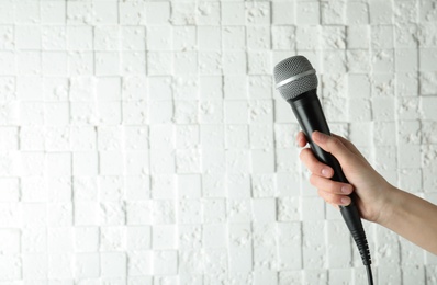 Photo of Woman holding modern microphone near white wall, closeup. Space for text