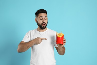 Emotional young man with French fries on light blue background