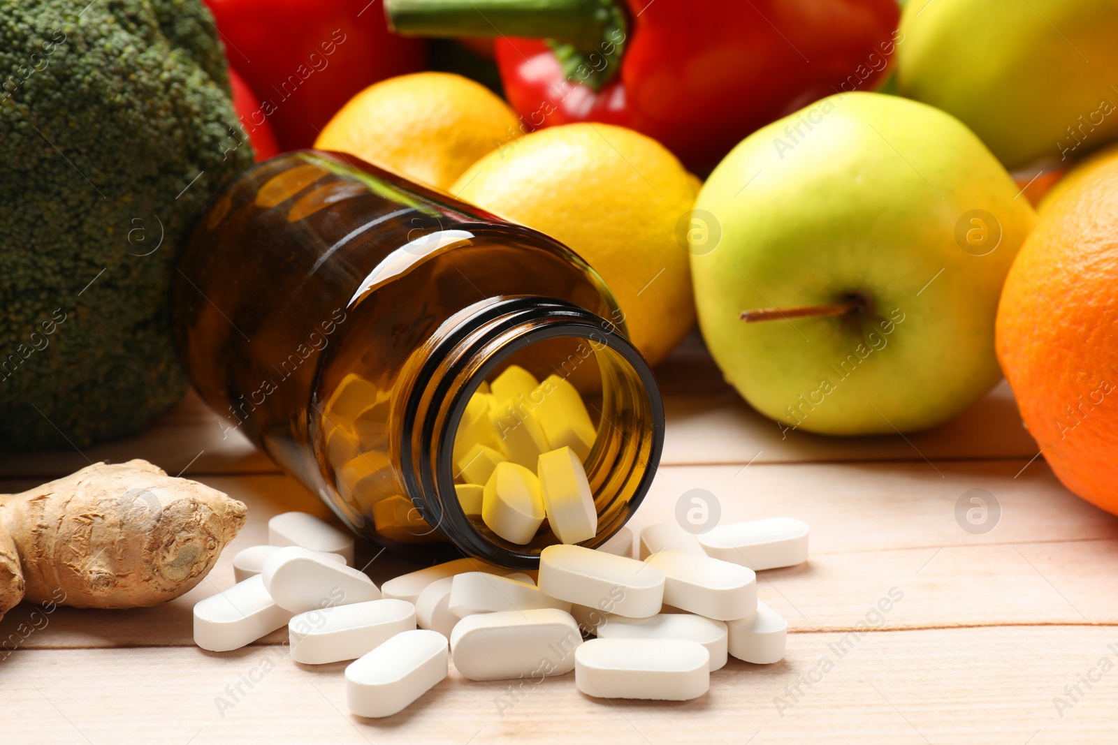 Photo of Dietary supplements. Overturned bottle with pills near food products on light wooden table