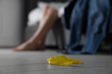 Photo of Woman sitting on bed and unrolled condom indoors, closeup. Safe sex