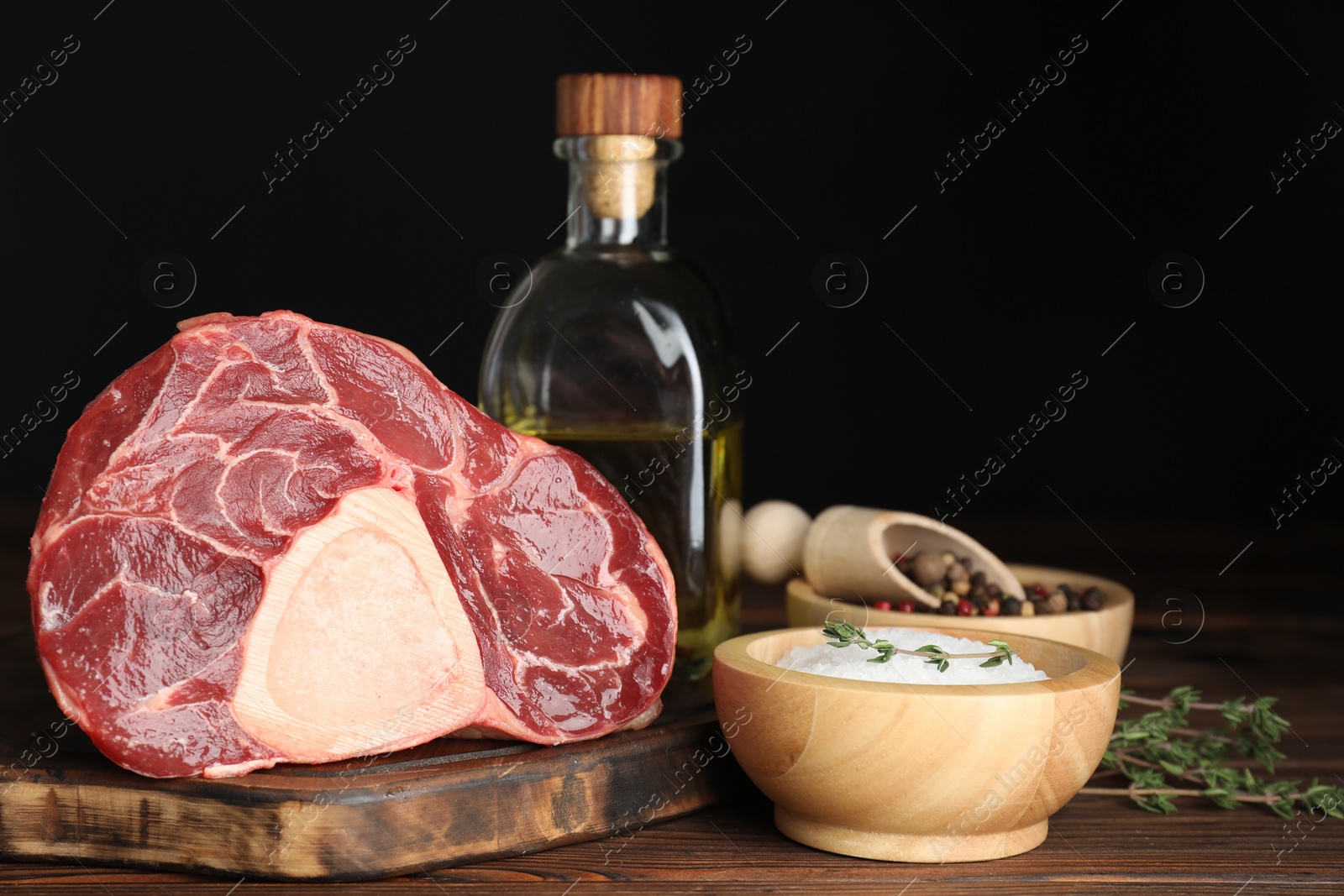 Photo of Piece of raw beef meat, thyme, oil and spices on wooden table against black background, closeup