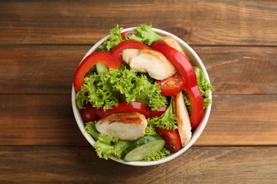 Delicious salad with chicken and vegetables on wooden table, top view